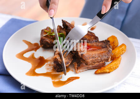 Young woman eating delicious ribs in restaurant Stock Photo