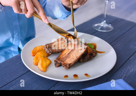 Young woman eating delicious ribs in restaurant Stock Photo