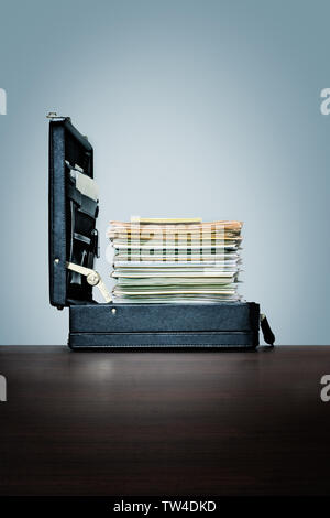 Compusive overwork, workaholic. Stack of files and folders in briefcase. on dark wood desk with blue background Stock Photo