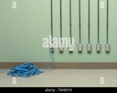 Blue coiled electric extension cord plugged into choice of AC outlets on green wall. Stock Photo