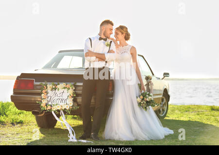 Happy wedding couple near decorated car on shore Stock Photo