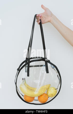 Plastic transparent shopping bag. Stylish reusable string bag with different fruits. Bananas, oranges, lemons in a transparent bag in the hand of a gi Stock Photo