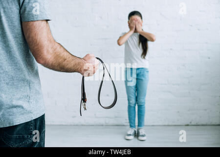 partial view of abusive father holding belt and scared daughter at home Stock Photo