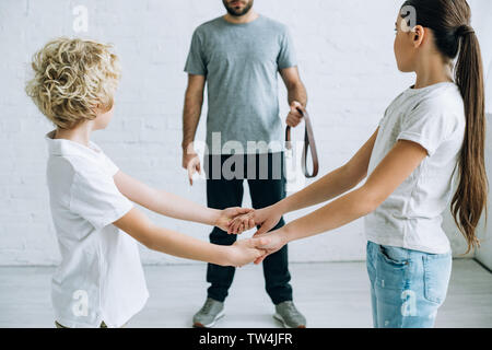 partial view of abusive father with belt and kids holding hands Stock Photo