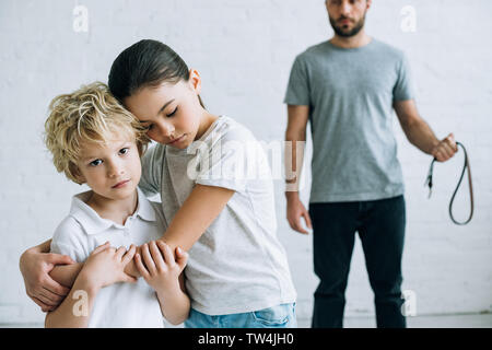 partial view of abusive father with belt and embracing kids at home Stock Photo