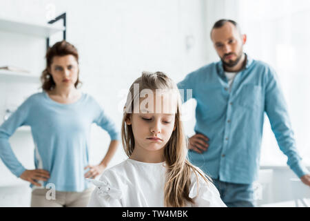 selective focus of upset child near sad parents standing at home Stock Photo
