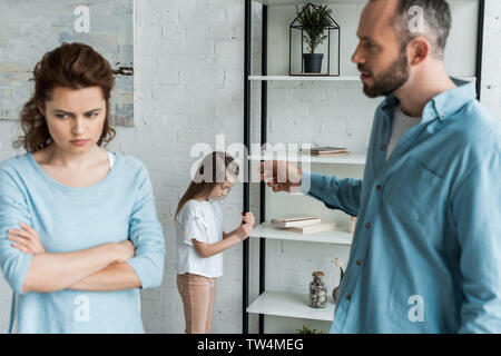selective focus of upset kid standing near rack while father pointing with finger near mother Stock Photo