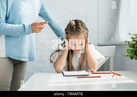 cropped view of mother standing near scared kid with closed eyes covering ears Stock Photo
