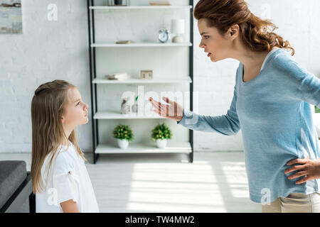 frustrated mother standing with hand on hip and gesturing near daughter Stock Photo
