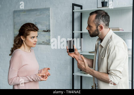 upset man pointing with finger at smartphone with blank screen near woman Stock Photo
