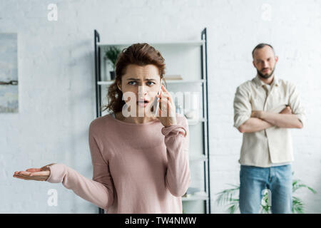 selective focus of upset woman talking on smartphone near man Stock Photo