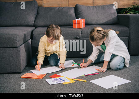 brother and sister sitting on floor and drawing on white paper sheets Stock Photo
