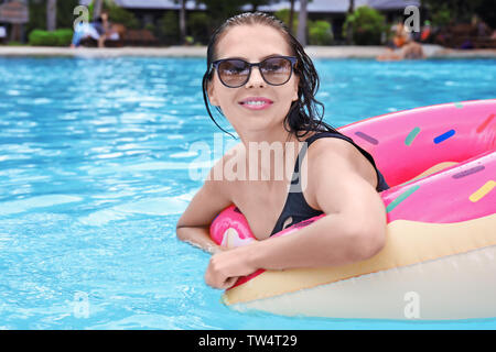 Beautiful young woman with inflatable donut in swimming pool Stock Photo