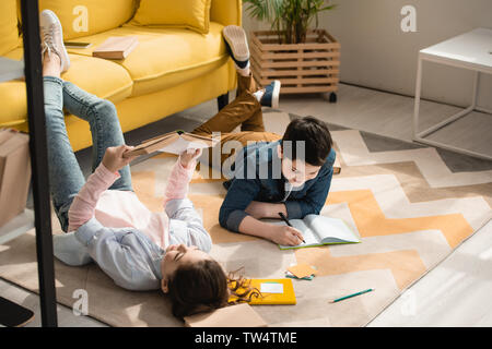 adorable kids lying on floor at home and doing schoolwork together Stock Photo
