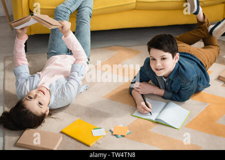 cheerful kids lying on floor at home and doing schoolwork together Stock Photo
