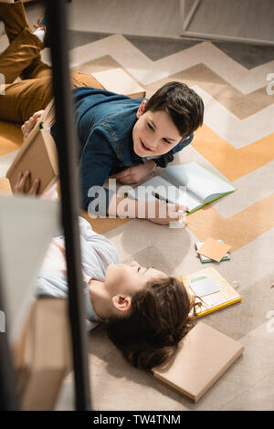 high angle view of cute brother and sister lying on floor and doing homework Stock Photo