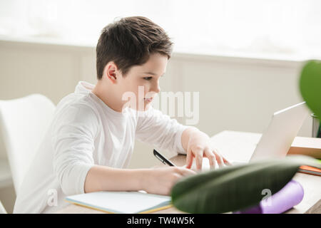 attentive writing in notebook and using laptop while doing schoolwork at home Stock Photo