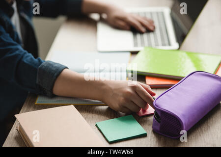 cropped view of schoolboy using laptop while sitting at desk with copy books and doing homework Stock Photo