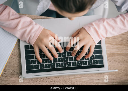 cropped view of schoolkid using laptop while sitting at desk and doing homework Stock Photo