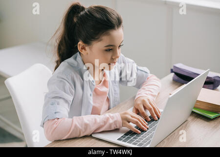 attentive schoolchild using laptop while sitting at desk and doing homework Stock Photo