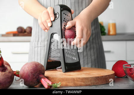 Woman grating beetroot in kitchen Stock Photo