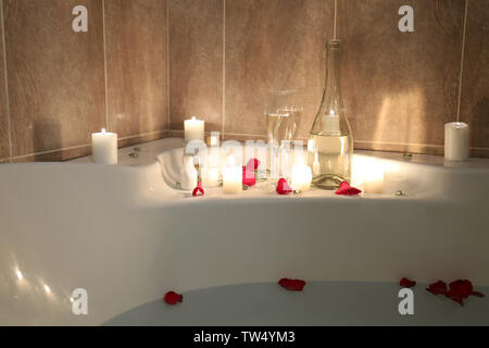 Two glasses of alcoholic drink with candles on bathtub filled with water and rose petals Stock Photo