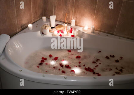 Spa accessories and candles on bathtub filled with foam and rose