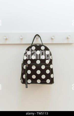 black polka dot backpack. on a hanger in the closet. A backpack hangs on a hook in a shop fitting room. sale of backpacks and bags. Stock Photo