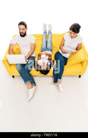 overhead view of kid lying on sofa and holding smartphone near latin parents using gadgets isolated on white Stock Photo
