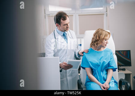 selective focus of doctor holding digital tablet and touching shoulder of upset woman Stock Photo