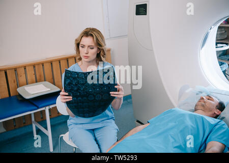 attentive radiologist examining radiology diagnosis near patient lying on mri scanner bed Stock Photo