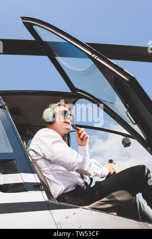 low angle view of Pilot in sunglasses and headset sitting in helicopter cabin Stock Photo