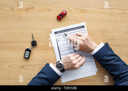 top view of car dealer holding pen near document with new car loan application form lettering, toy car and car key Stock Photo