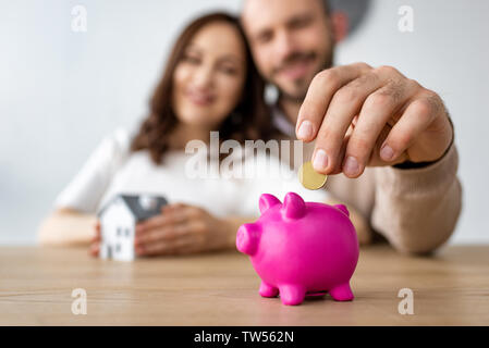 selective focus of man putting coin in pink piggy bank and cheerful woman Stock Photo