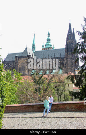 Prague, Czech Republic - May 2016: Lovely couple taking photo in park near the Gothic towers of St. Vitus Cathedral, immersed in spring young green fo Stock Photo