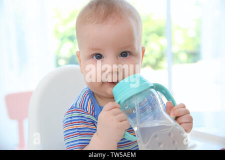 Cute baby drinking water from plastic bottle indoors Stock Photo