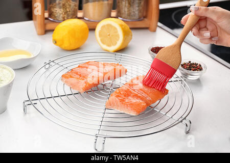 Woman applying oil on red fish fillet with silicone brush in kitchen Stock Photo