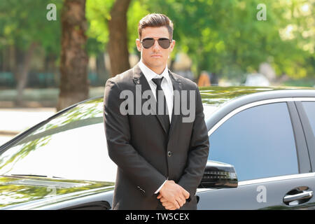 Handsome bodyguard near car outdoors Stock Photo