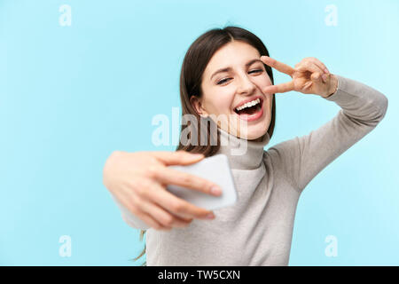 beautiful young caucasian woman taking a selfie, happy and smiling, isolated on blue background Stock Photo