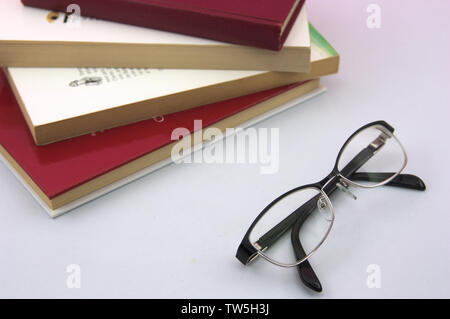 A pile of reading books and a pair of reading glasses close up on a white table Stock Photo