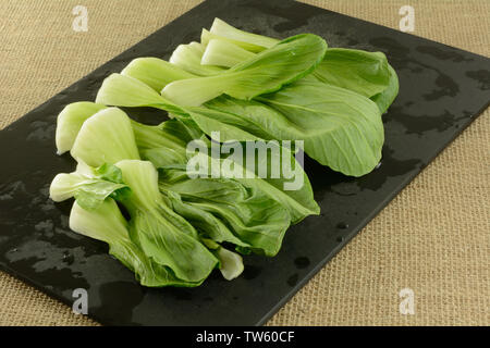 Freshly rinsed bok choy leaves on black cutting board Stock Photo