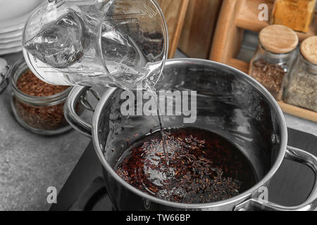 Pouring water into stewpot with boiling rice Stock Photo