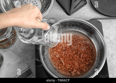 Woman pouring water into bowl with boiling rice Stock Photo