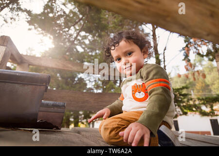 Two year old boy sitting in a tree house in a park smiling with a beautiful sunset behind in autumn Stock Photo