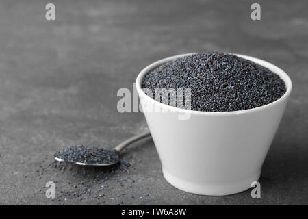 Ripe poppy seeds in ceramic bowl and metal spoon on grey background Stock Photo