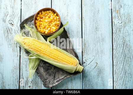 Corn cob and bowl with kernels on tray against wooden background Stock Photo