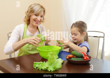 Cute little girl and her grandmother cooking on table Stock Photo