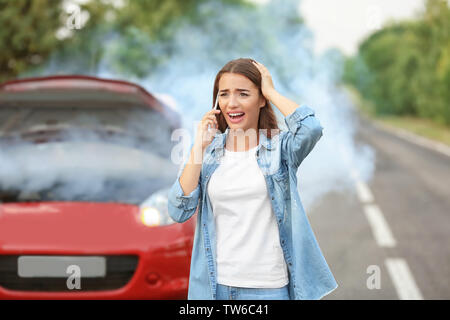 Upset young woman with cell phone near broken car Stock Photo