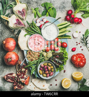 Vegetarian snack board. Flat-lay of beetroot hummus, yogurt dip, kinoa salad, olives, beens, vegetables and fruit with flatbread over grey concrete ba Stock Photo