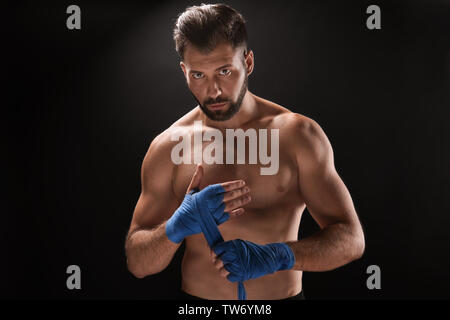 Male boxer applying wrist wraps on dark background Stock Photo